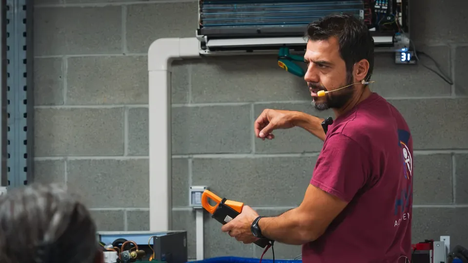 Docente HVAC Academy Italia con una pinza di misura davanti a un climatizzatore didattico aperto